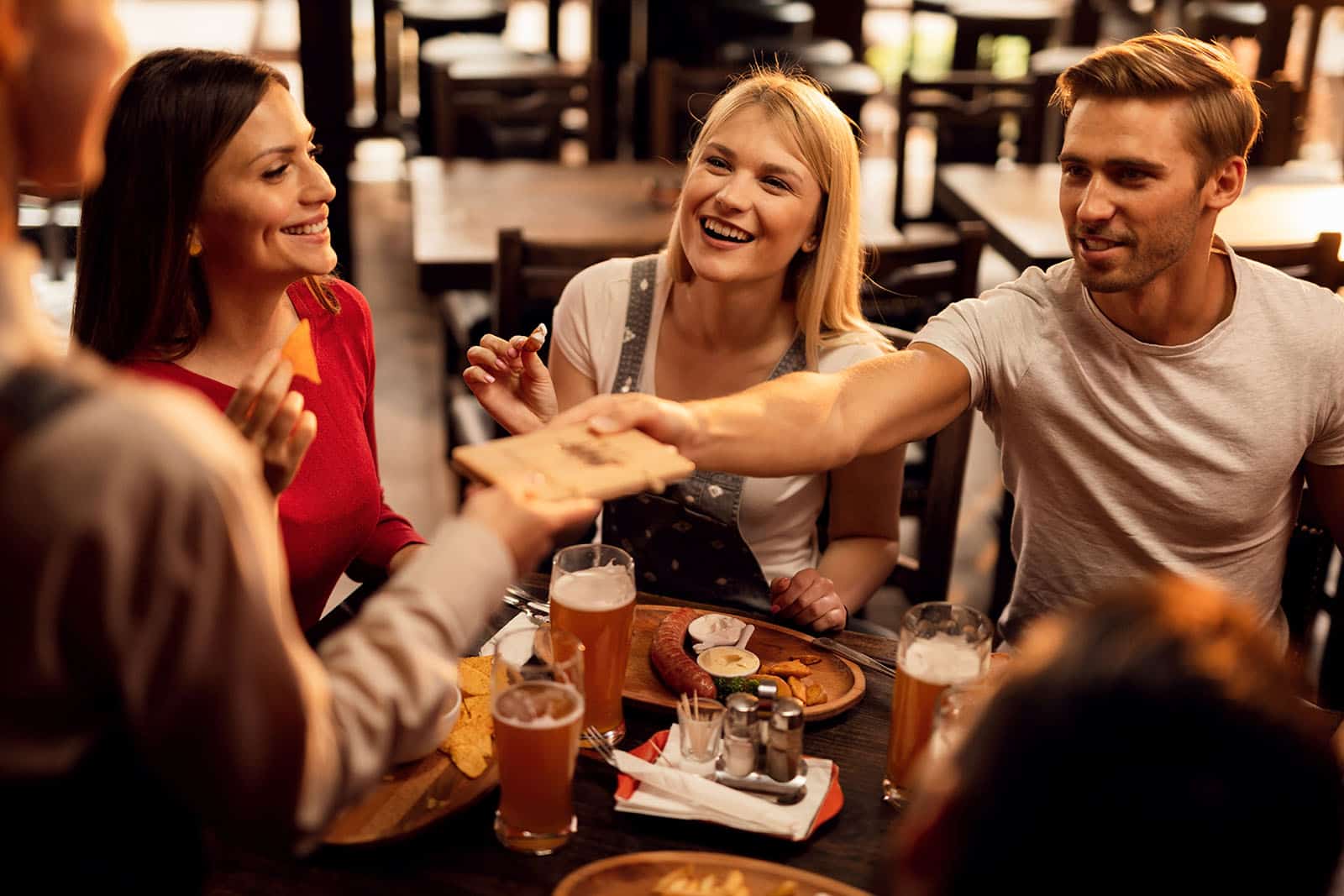 Group of happy friends paying restaurant check to a waiter